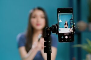 A smartphone mounted on a tripod, recording short videos of a young woman applying makeup.