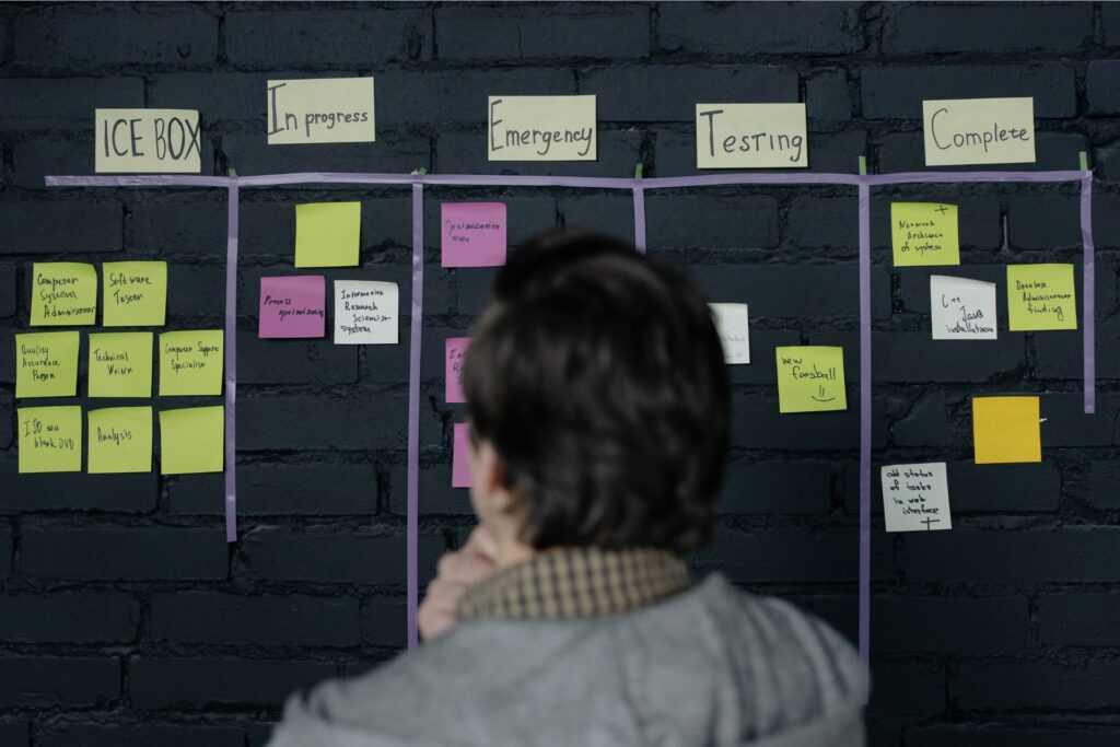 A person reviews a Kanban board organizing tasks across stages with sticky notes, showcasing tools to manage multiple social media accounts by prioritizing and tracking progress.