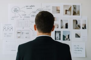 Person in a business suit looks at a wall covered with papers and images showing project plans and website designs, representing work on building a strong online reputation.