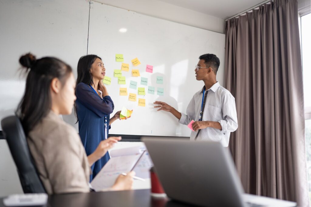 Team brainstorming digital marketing strategy mistakes around whiteboard with sticky notes on creativity, teamwork, and business ideas in collaborative office meeting.