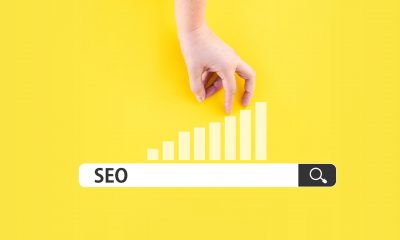 A hand points to an upward bar graph above a search bar with "SEO" typed in against a bright yellow background, symbolizing growth from debunking SEO myths.