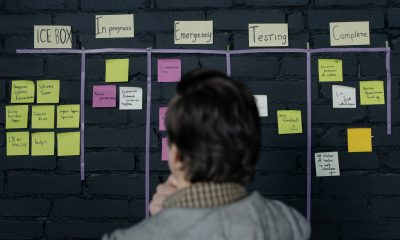 A person reviews a Kanban board organizing tasks across stages with sticky notes, showcasing tools to manage multiple social media accounts by prioritizing and tracking progress.
