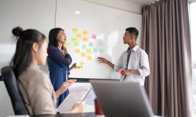 Team brainstorming digital marketing strategy mistakes around whiteboard with sticky notes on creativity, teamwork, and business ideas in collaborative office meeting.